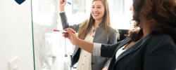 two smiling women collaborating in front of a whiteboard
