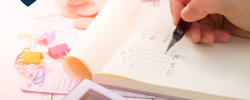 a warmly-lit desk with a notepad, calculator, money and paperclips as well as a pair of hands calculating and drawing charts on the notepad